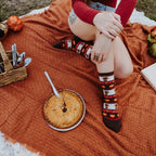 Two women in fall sweaters share pie at a Thanksgiving spread, modeling Gobble Gobble socks in Ivory Heather together. [lf]