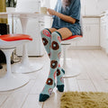 A pair of Go Nuts For Donuts socks in Blue Heather crossed on a rug beside a pink donut box. [lf]