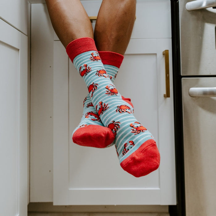 A pair of Crabby Crew socks in Blue Heather stretched across a kayak deck, the crab motifs vivid in the sun. [lf]
