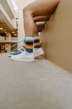 A close-up of Progress Stripes socks in Multi resting on a yoga mat after a workout, paired with athletic sneakers. [lf]