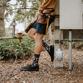 A friend hands a tool across a workbench while modeling Can You Fix It? socks in Navy Heather with hammer and saw graphics. [lf]