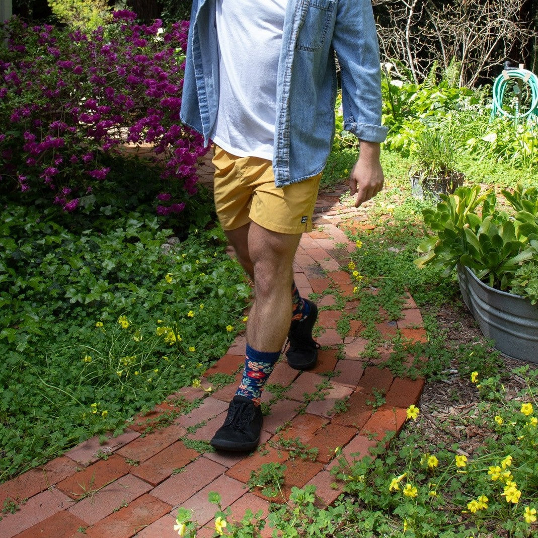 A close-up of Wild Flowers socks in Navy Heather featuring wildflower illustrations, on a person walking through a meadow. [lf]