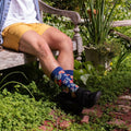 A pair of Wild Flowers socks in Navy Heather crossed on a picnic blanket among meadow grasses. [lf]