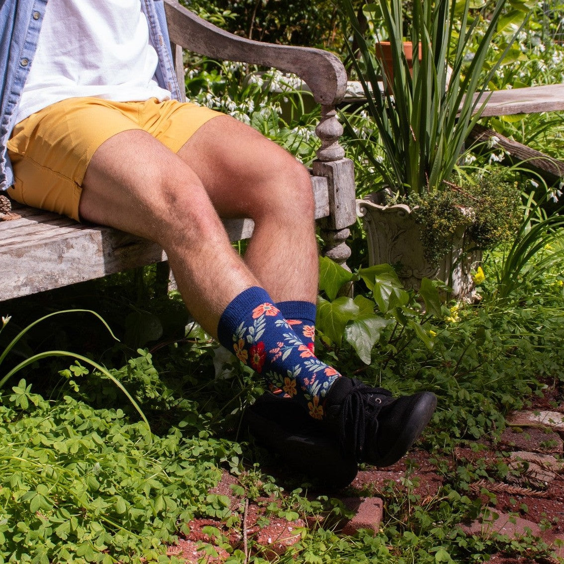 A pair of Wild Flowers socks in Navy Heather crossed on a picnic blanket among meadow grasses. [lf]