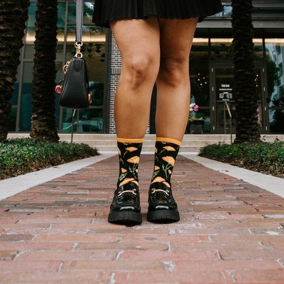A close-up of California Poppies socks in Black featuring California poppies, on a person in a sunny meadow of orange wildflowers. [lf]
