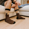 A pair of Dog Gone Stripes Bamboo socks in Hemp crossed on a porch beside a chewed tennis ball. [lf]