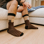 A pair of Dog Gone Stripes Bamboo socks in Hemp crossed on a porch beside a chewed tennis ball. [lf]