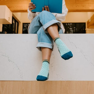 A close-up of Pin Dot socks in Teal Heather featuring tiny pin-dot patterns, paired with loafers on a polished wood floor. [lf]