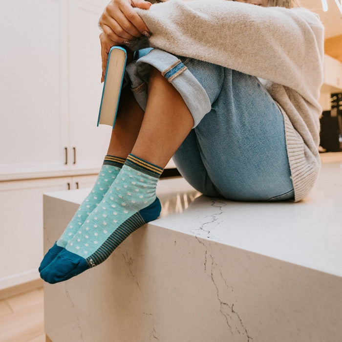 A pair of Pin Dot socks in Teal Heather stretched across a desk strewn with files and a fountain pen. [lf]