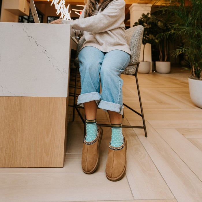 A pair of Pin Dot socks in Teal Heather on crossed feet at a coffee shop counter. [lf]
