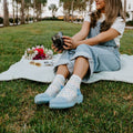 A close-up of Spectrum of Love socks in Ivory on a wooden bench beside a vase of mixed wildflowers. [lf]