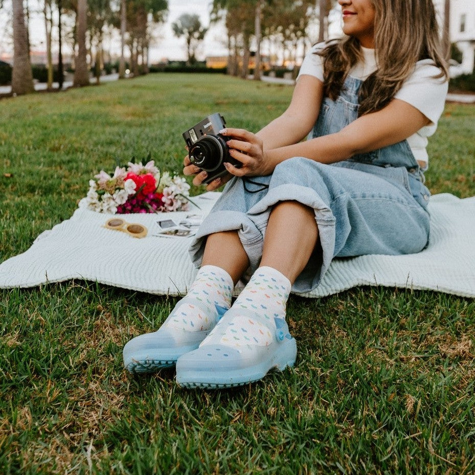 A close-up of Spectrum of Love socks in Ivory on a wooden bench beside a vase of mixed wildflowers. [lf]