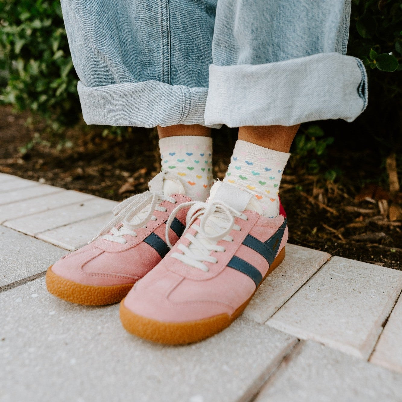 A couple laughs together on a porch swing, both modeling Spectrum of Love socks in Ivory with rainbow love motifs. [lf]