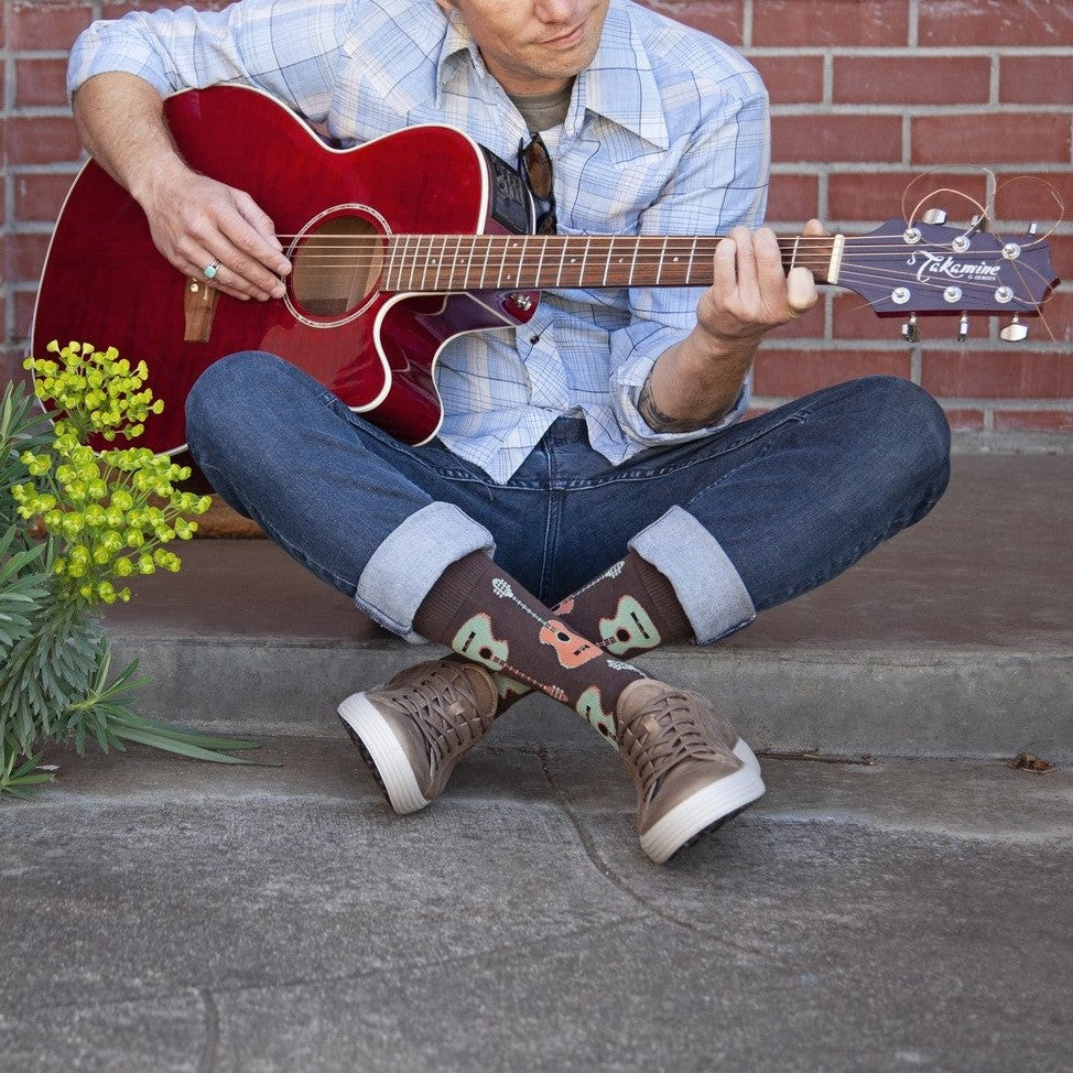 Guitars XL socks featuring guitars shown on a musician seated cross-legged on a porch step beside yellow flowers. [lf]