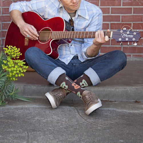 Guitars XL socks featuring guitars shown on a musician seated cross-legged on a porch step beside yellow flowers. [lf]