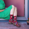 Ugly Sweaters red socks with cheesy Christmas sweater prints shown on a smiling couple in a green dress and floral shirt. [lf]