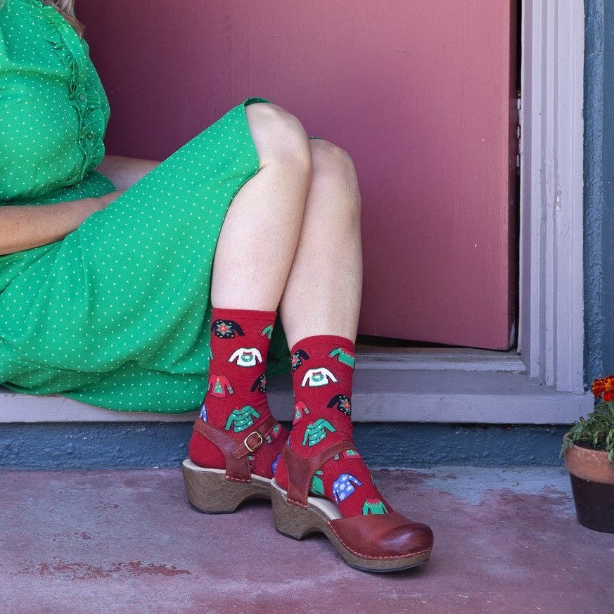 Ugly Sweaters red socks with cheesy Christmas sweater prints shown on a smiling couple in a green dress and floral shirt. [lf]