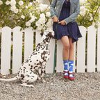 A woman in a navy dress holds her dalmatian on a leash beside white roses, wearing Slightly Cloudy blue cloud-print socks with bright red platform sandals. [lf]