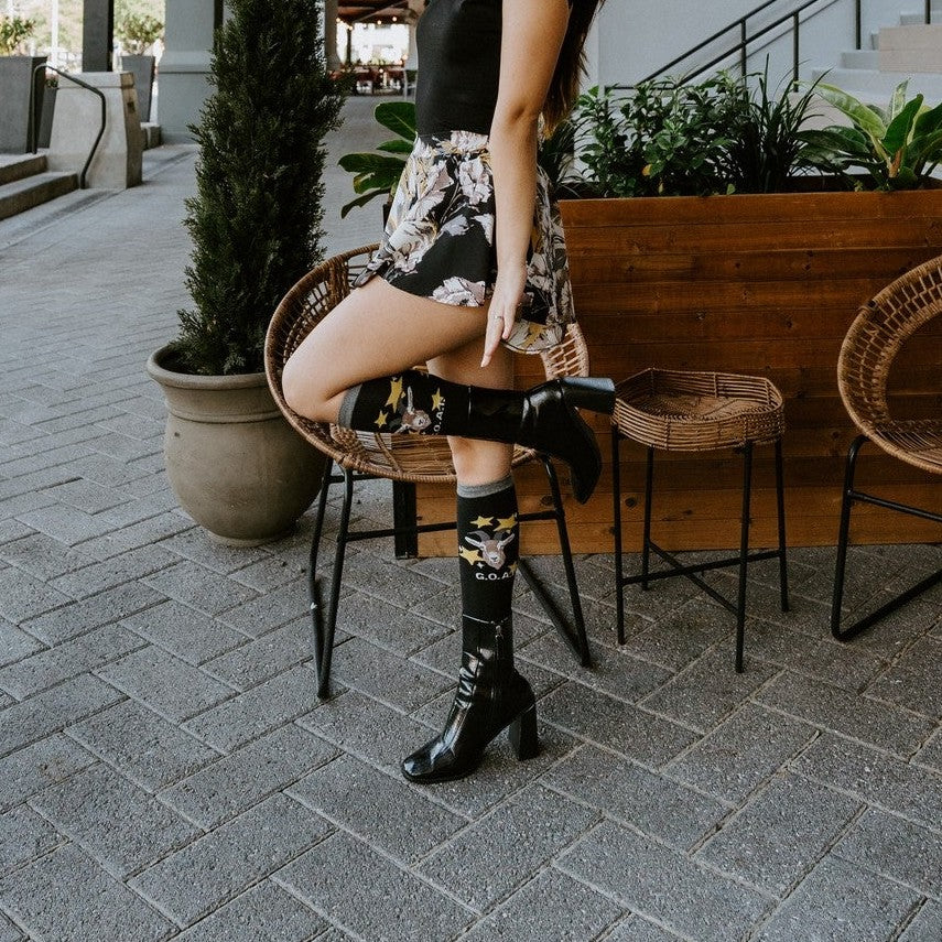 Goat socks worn with patent black booties and a floral skirt on a sunny exterior porch. [lf]