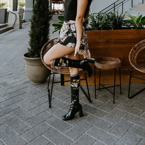 Goat socks worn with patent black booties and a floral skirt on a sunny exterior porch. [lf]