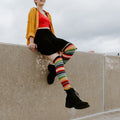 Mexican Serape multicolor striped knee-high socks photographed against an overcast urban sky. [lf]