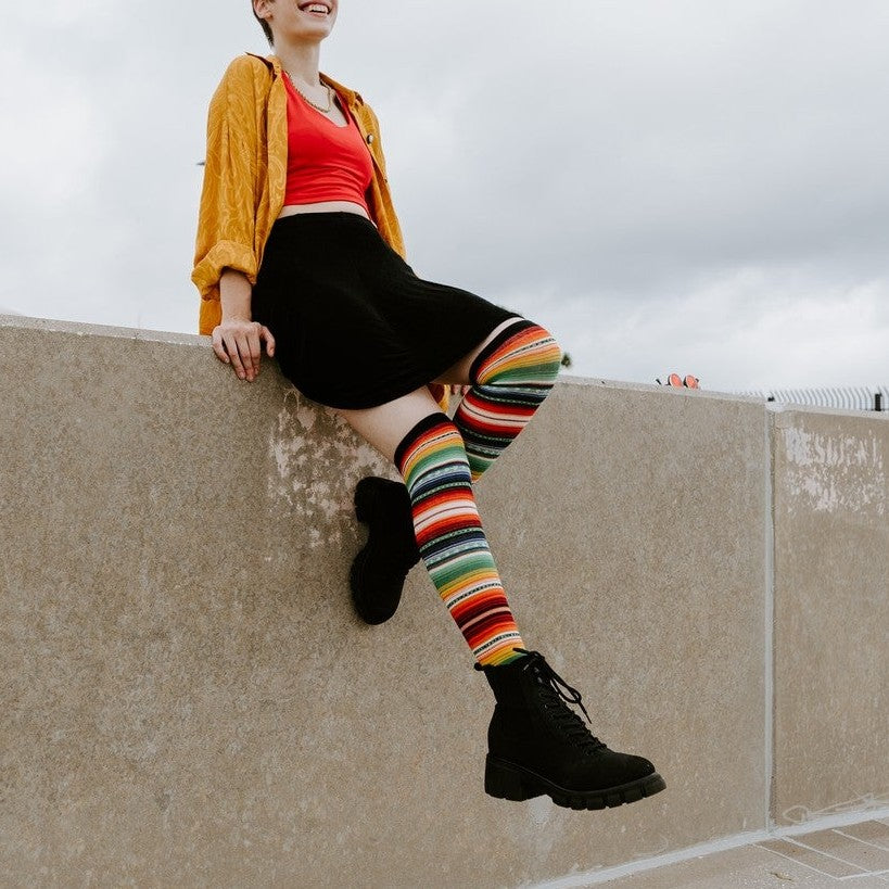 Mexican Serape multicolor striped knee-high socks photographed against an overcast urban sky. [lf]