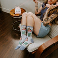 Cat Calls blue socks with cute cats and retro phones shown on a model relaxing in a modern reading chair. [lf]