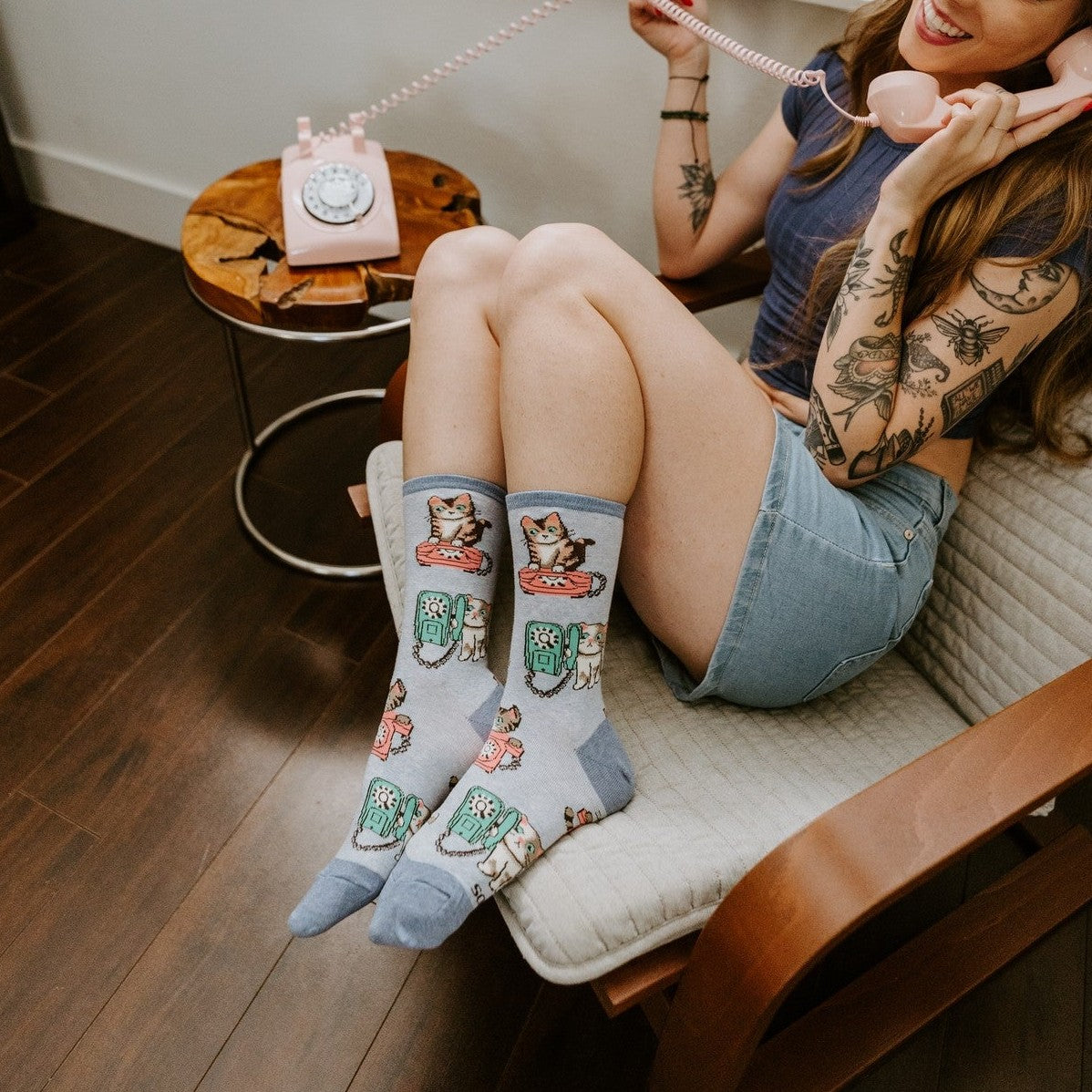 Cat Calls blue socks with cute cats and retro phones shown on a model relaxing in a modern reading chair. [lf]