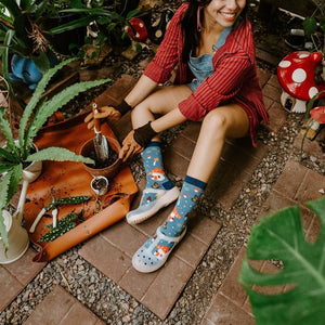 Magical Forest blue socks shown in styled detail surrounded by greenery and mushroom planters. [lf]