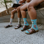 Socks And Sandals shown in styled detail on a couple's feet, leather Birkenstock-style sandals layered over striped knit. [lf]