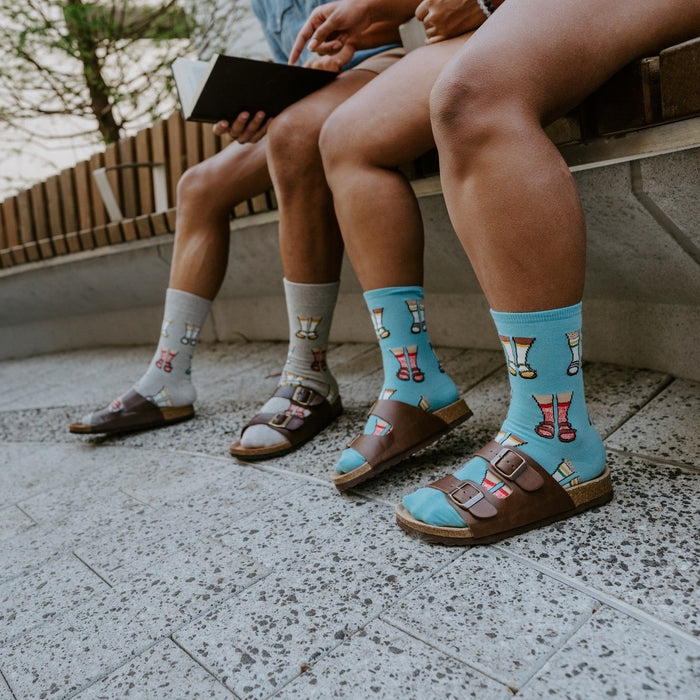 Socks And Sandals shown in styled detail on a couple's feet, leather Birkenstock-style sandals layered over striped knit. [lf]