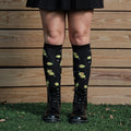 Cocktail Olives knee-high socks photographed on a model with a backpack against a fence backdrop. [lf]