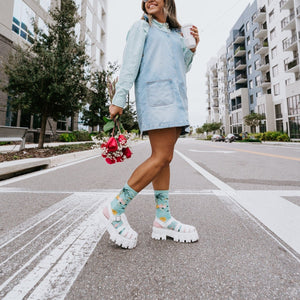 Bird's Eye View tropical themed socks worn on a sunny urban street with palm trees in the background. [lf]