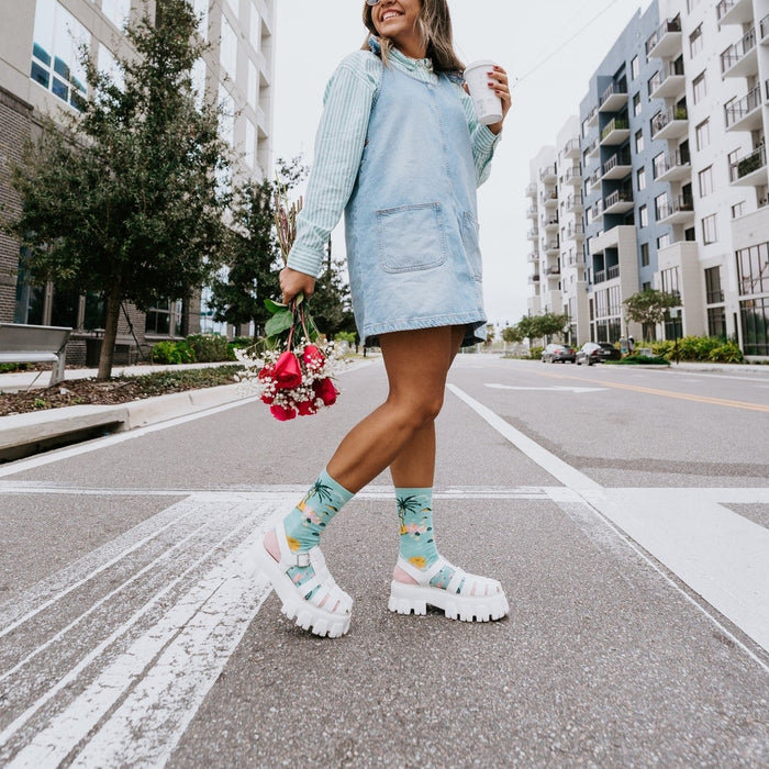 Bird's Eye View tropical themed socks worn on a sunny urban street with palm trees in the background. [lf]
