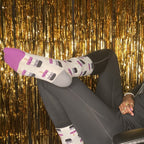 The same model rests a hand on her chin and kicks her feet over the chair arm, the purple-banded popsicle prints of her Asexual Pops socks pointed toward the camera in front of a wall of gold fringe. [lf]