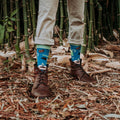 A horizontal shoes-up shot in bamboo undergrowth highlights Green Thumb Bamboo in Blue socks worn with cuffed khakis and brown lace-up boots. [lf]
