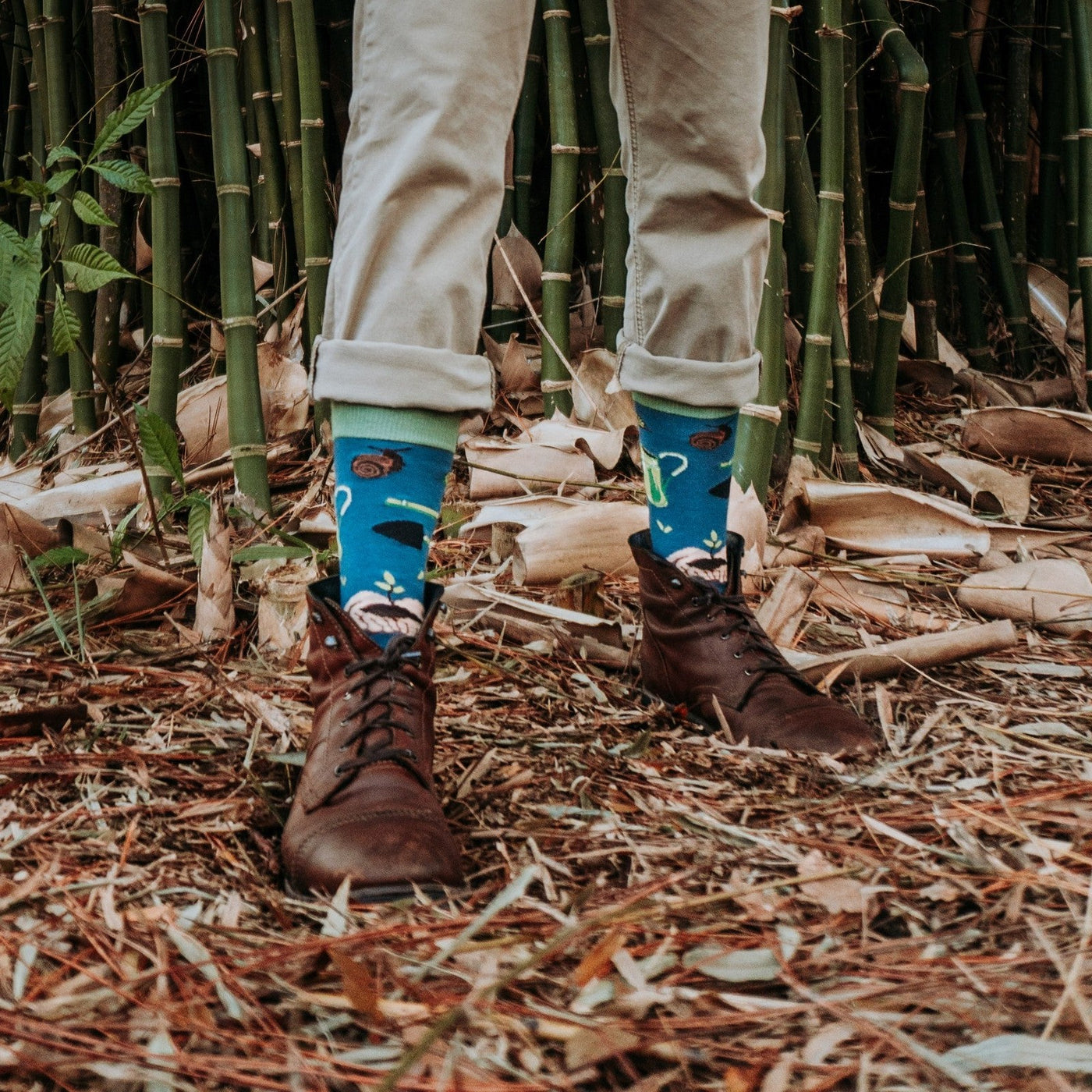 A horizontal shoes-up shot in bamboo undergrowth highlights Green Thumb Bamboo in Blue socks worn with cuffed khakis and brown lace-up boots. [lf]