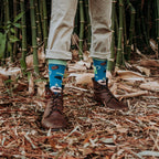 A horizontal shoes-up shot in bamboo undergrowth highlights Green Thumb Bamboo in Blue socks worn with cuffed khakis and brown lace-up boots. [lf]
