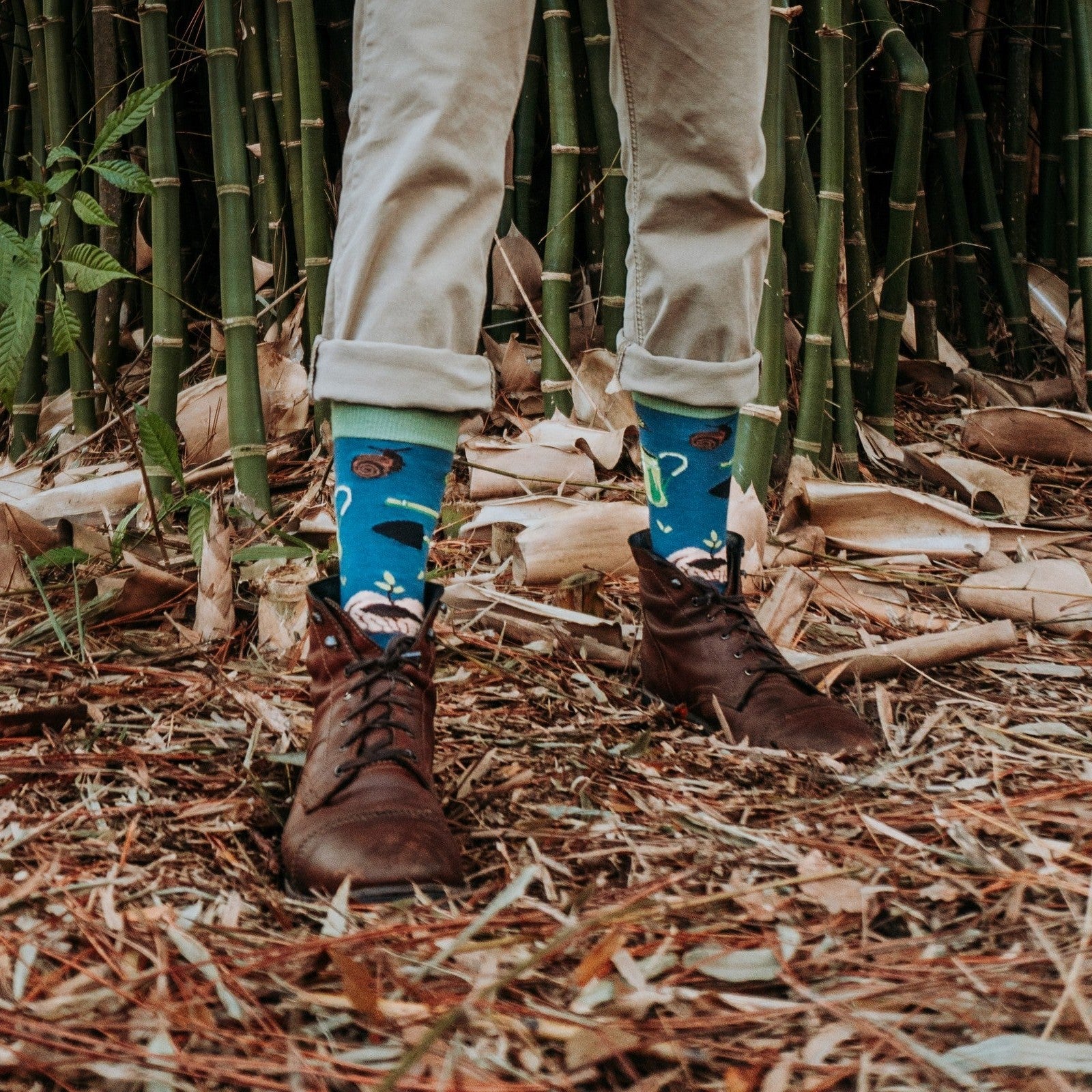 A horizontal shoes-up shot in bamboo undergrowth highlights Green Thumb Bamboo in Blue socks worn with cuffed khakis and brown lace-up boots. [lf]