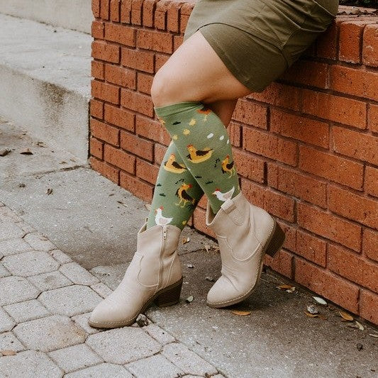 Confident lean against the brick wall with hand on hip in a town square, the printed roosters and hens of the Chicken Ranch socks on full display. [lf]