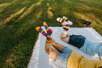 Wider angle of the picnic scene, legs raised on the blanket so the Progress Stripes and Pride Stripes socks catch the afternoon sun. [lf]