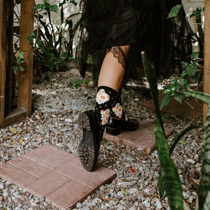 Model in orange top and black tulle skirt poses in a Halloween-decorated garden with a carved pumpkin, wearing Flower Ghosts socks in Black. [lf]