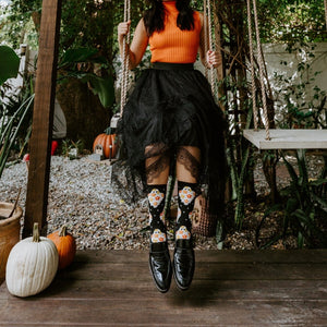 Model on a wooden swing surrounded by greenery and pumpkins, kicking out her feet in Flower Ghosts socks in Black. [lf]