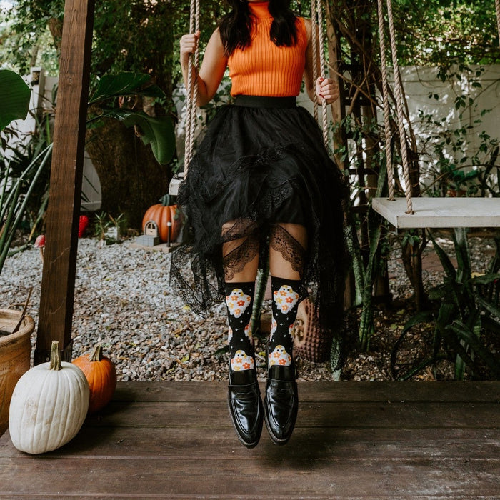 Model on a wooden swing surrounded by greenery and pumpkins, kicking out her feet in Flower Ghosts socks in Black. [lf]
