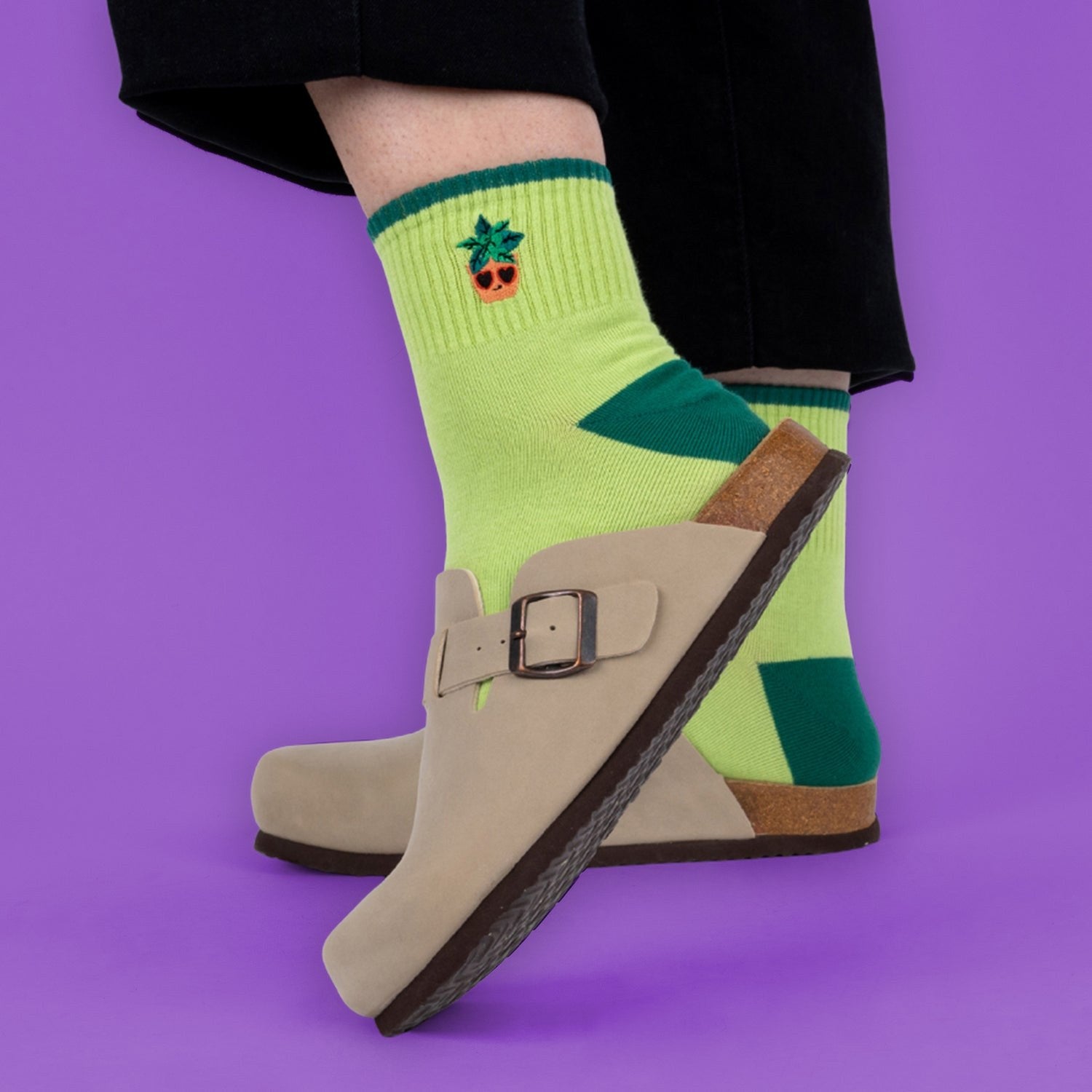 [lf] Lime green socks with a pineapple wearing sunglasses, paired with beige clogs on a purple background.