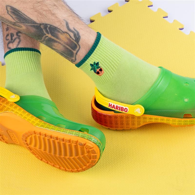 [lf] Lime green socks with pineapple embroidery, worn with Haribo Crocs on a yellow mat.