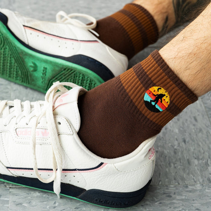 [lf] Brown striped socks with colorful Bigfoot patch worn by model in white sneakers.