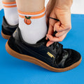 [lf] Person tying black Puma sneakers, wearing white socks with orange stripes and a peach embroidery.