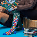 [lf] People relaxing, reading books, wearing green "Booked for the Weekend" socks with colorful book stacks.