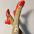 [lf] Legs crossed, a model wears red patent shoes and olive socks with deer and mushroom patterns.